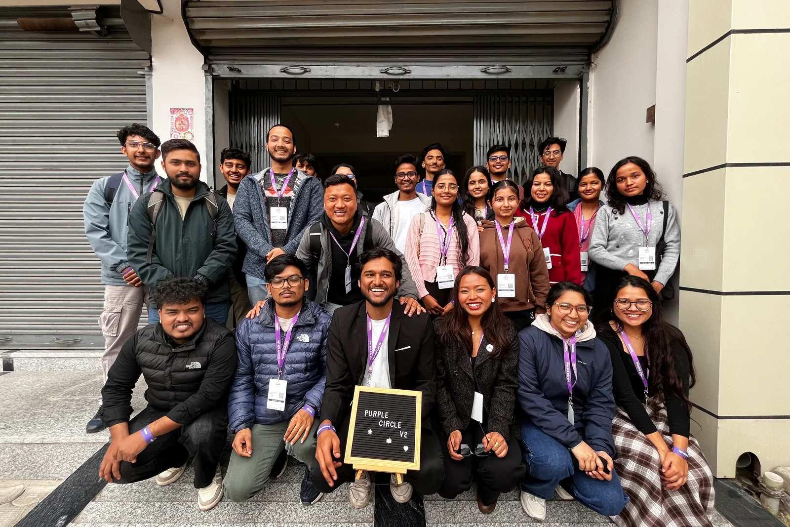 The Version 2 group on the venue steps in Bharatpur, holding a board reading Purple Circle V2