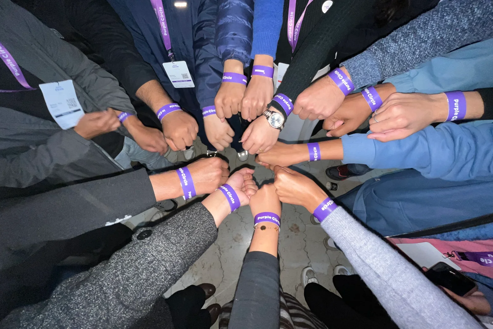 Attendees at Version 2 standing in a circle, Purple Circle wristbands on, fists together in the middle